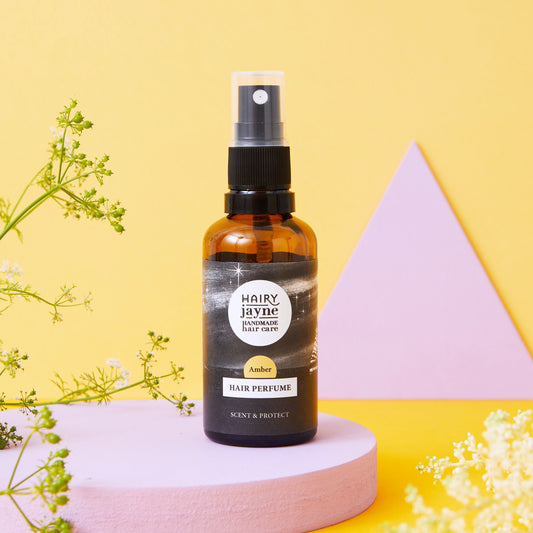 Hair perfume bottle labeled 'Hairy Jayne' on a yellow background with geometric shapes and greenery.