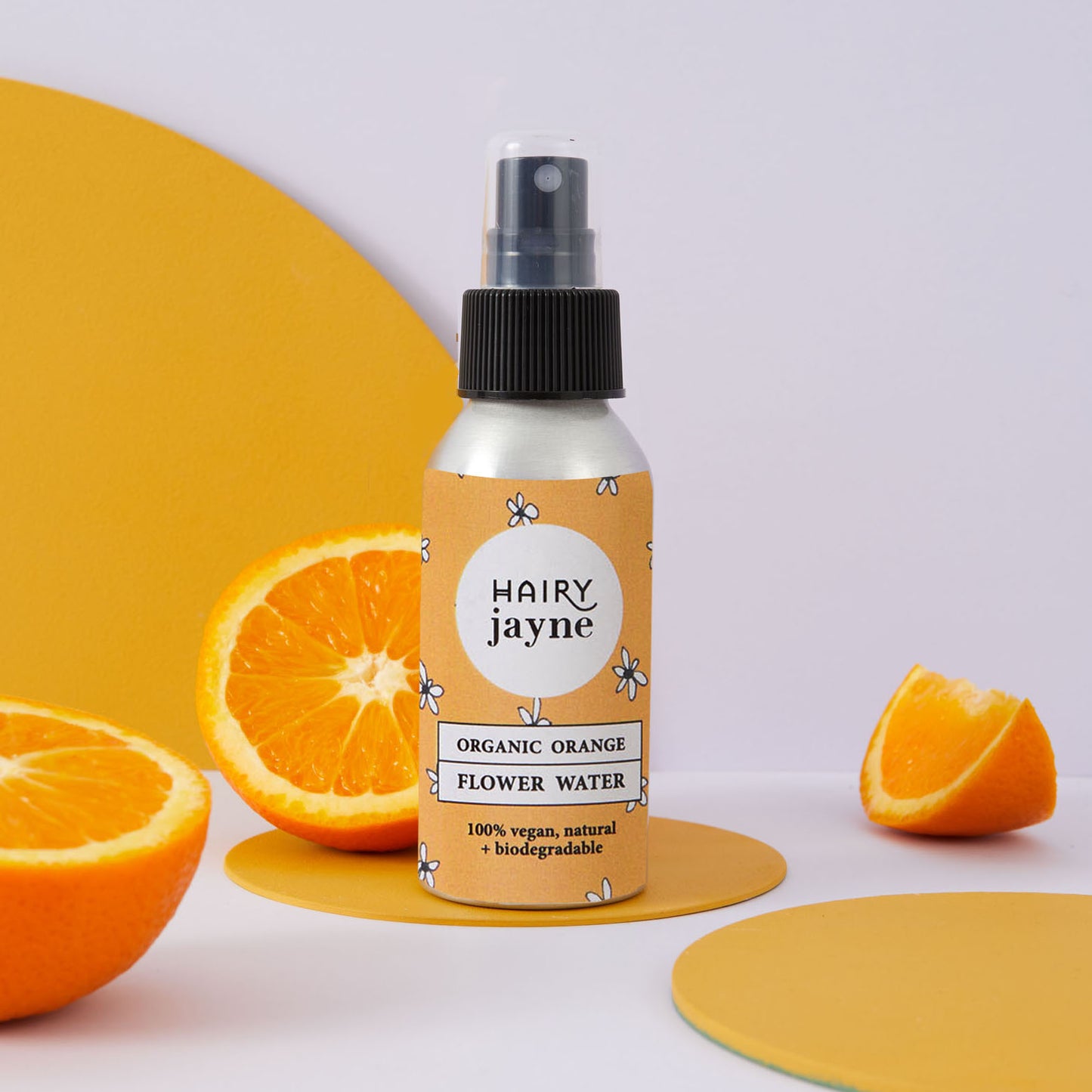 Aluminium spray bottle of Hairy Jayne organic orange flower water with oranges on a light background