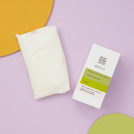 Hairy Jayne cream conditioner refill pouch and packaging on a purple background with orange and green props