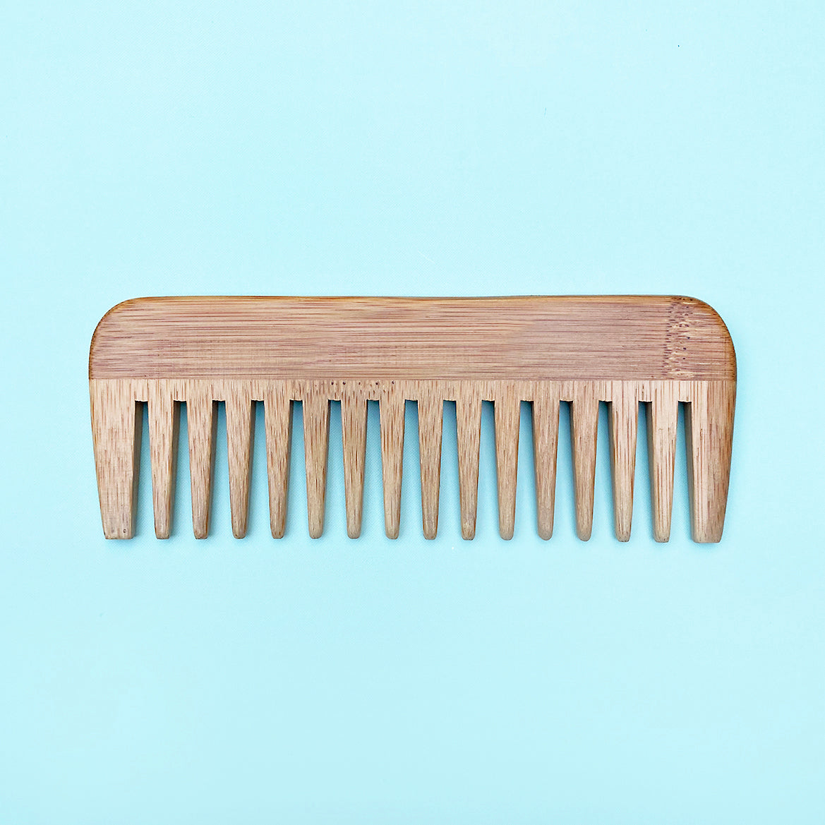 A light natural bamboo hair comb with wide teeth, shown flat against a solid light blue background.