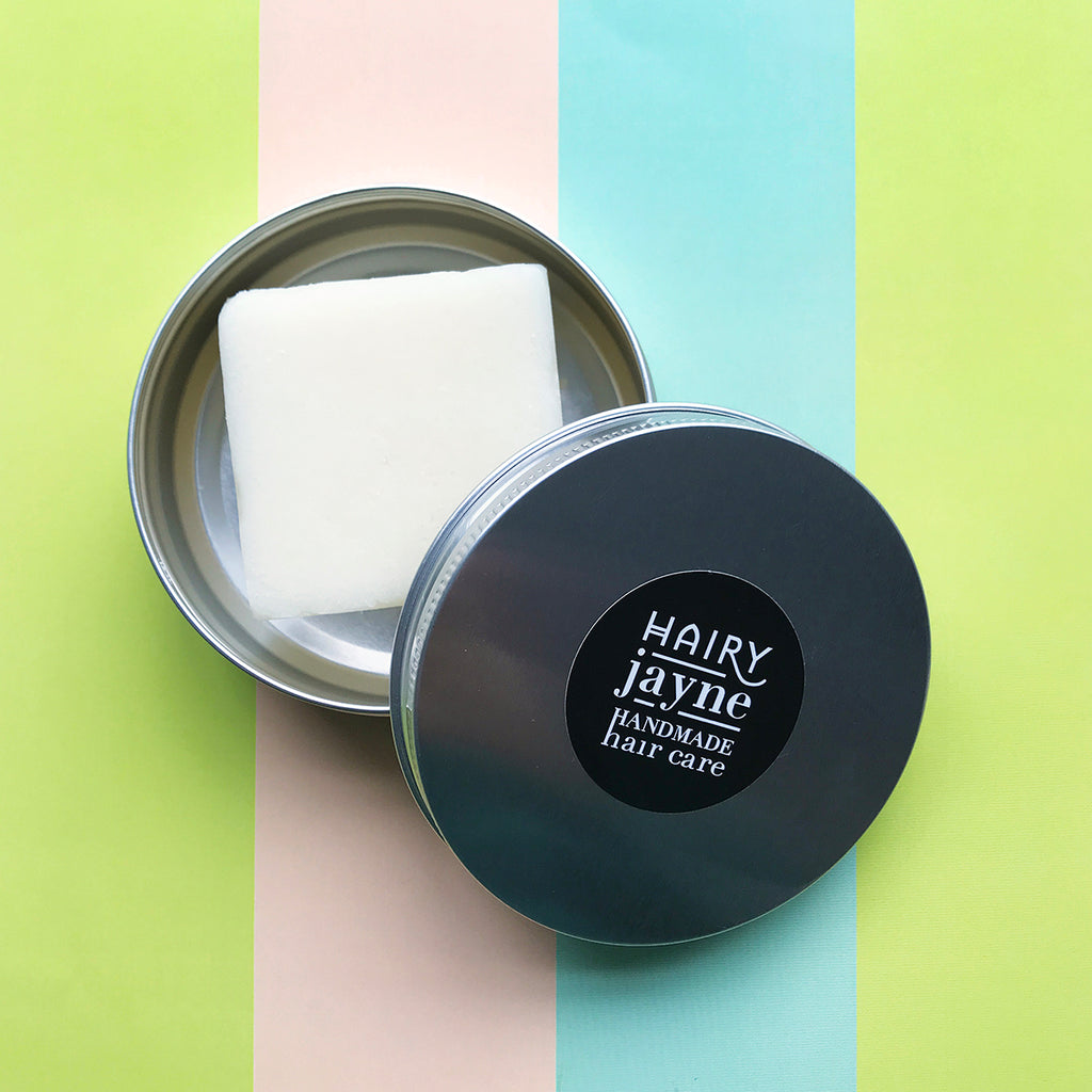 plastic free conditioner bar in an aluminium travel tin with the lid resting on top. pastel coloured stripy background