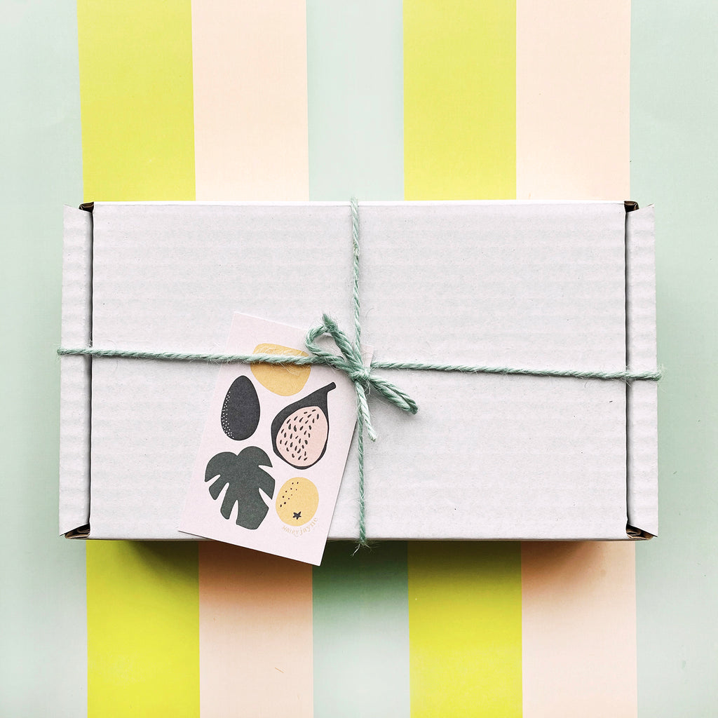 our gift wrap - a white cardboard box tied with mint twine with a card for gift message. the card has illustrations of fruit and a palm leaf